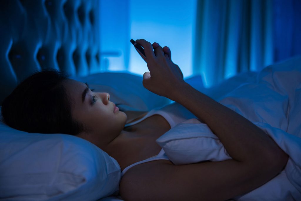 woman checking her phone in bed in the dark