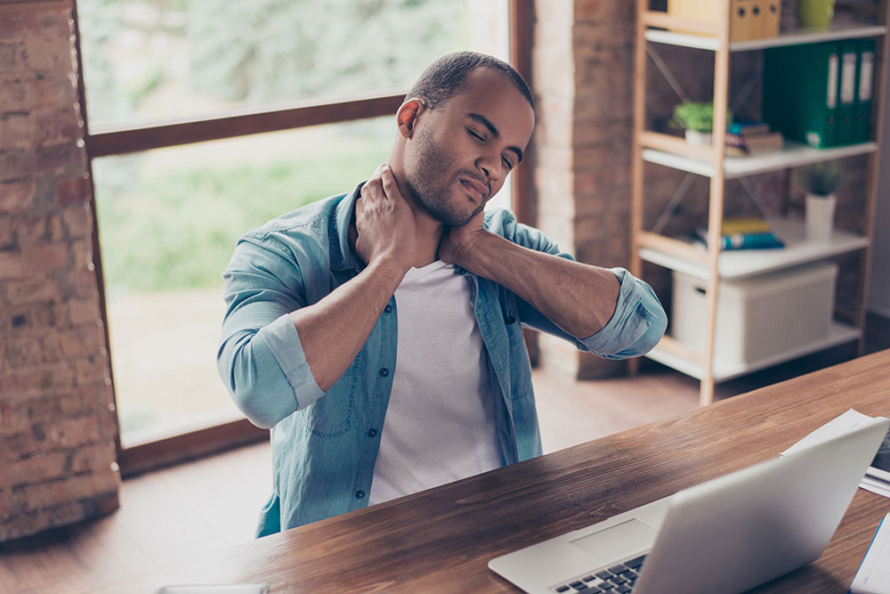 man sitting at desk, holding his neck in pain