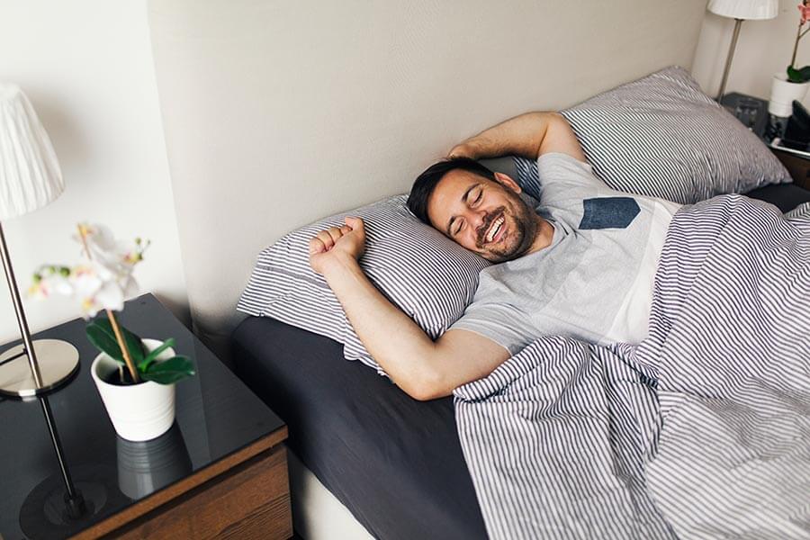 Smiling man stretching in bed after waking up