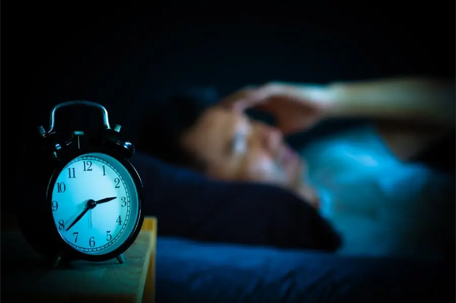 Man having trouble sleeping with an alarm clock in the foreground