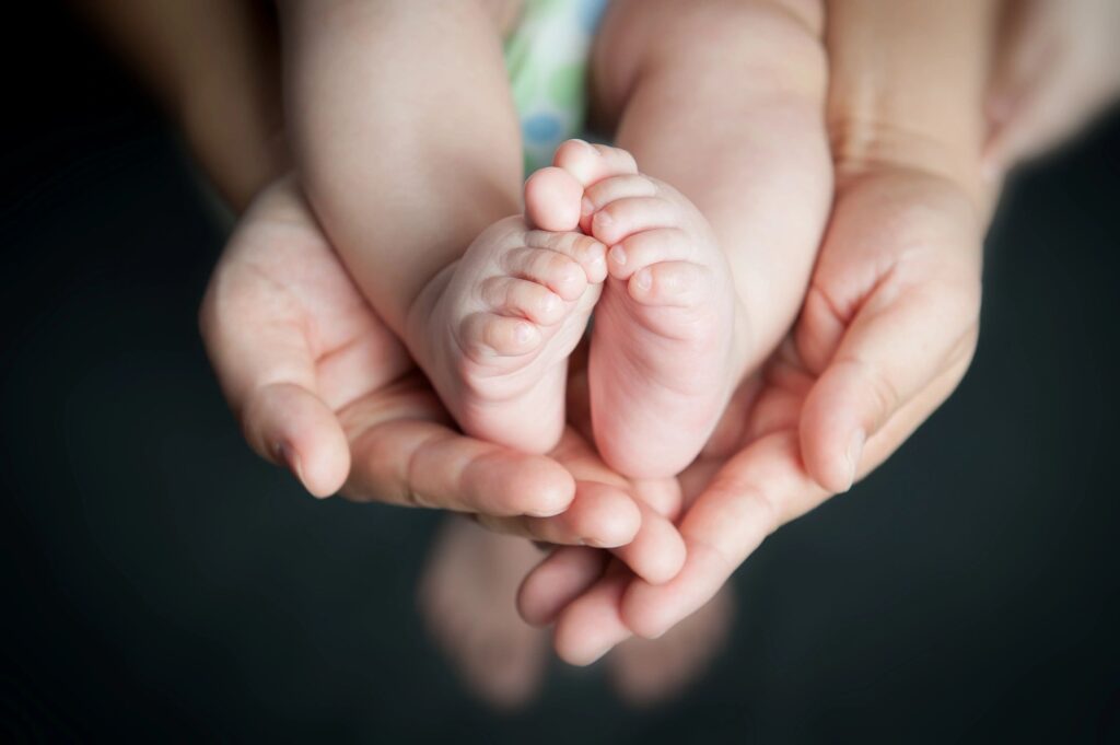 A newborn's feet is on top of a parent's hands